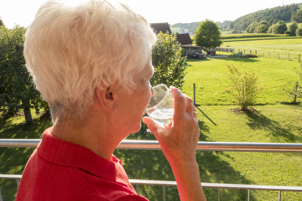 Senior citizen drinking a glass of water in the sun in the garden - Geriatric Nutrition and Hydration
